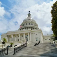 View of the United States Capitol with stairs and an American flag under a blue sky with clouds.