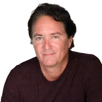 Middle-aged man with dark hair wearing a dark shirt smiling softly against a white background