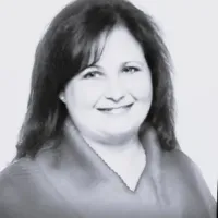 Smiling woman with dark hair wearing a shawl, looking at the camera in a grayscale portrait.