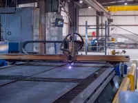 Industrial CNC plasma cutting machine cutting metal sheets in a factory workshop with safety barriers.