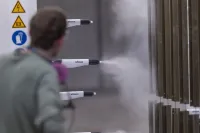 Person operating spray guns applying coating to metal panels in an industrial setting