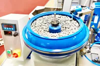 Industrial machine with a blue bowl containing small stones for grinding or polishing materials.