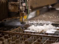 Industrial water jet cutting machine slicing through metal sheets with water spray and sparks