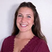 Smiling young woman with long brown hair wearing a maroon top against a white background