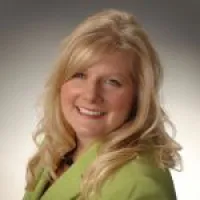 Smiling woman with long blonde hair wearing a green blazer against a neutral background
