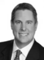 Smiling man in a suit and tie with short hair against a plain white background.