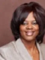 Portrait of a smiling woman with short dark hair wearing a light-colored blazer against a brown background