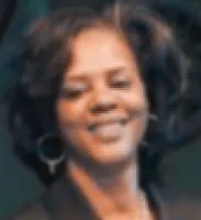 Smiling woman with curly hair and hoop earrings in a dark blurred background