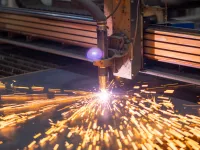 Industrial plasma cutting machine producing bright sparks while cutting metal sheet on factory floor
