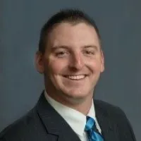 Smiling man in business suit with blue tie against gray background, professional headshot portrait
