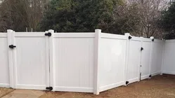 Sturdy white vinyl fence enclosing a yard, featuring a secure latch and green trees in the background.
