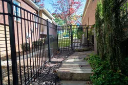 Serene backyard pathway leading to a gated area surrounded by greenery and brick walls.
