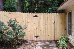 Wooden fence gate with black metal hinges next to house and rose bushes in garden