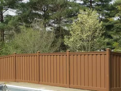 A brown wooden fence surrounding a pool with greenery in the background under a clear sky.