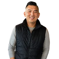 Smiling man wearing a black puffer vest over a gray long-sleeve shirt isolated on white background