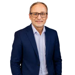 Smiling middle-aged man wearing glasses, a light blue shirt, and a navy blazer against a transparent background