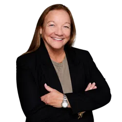 Smiling middle-aged woman with long hair wearing a black blazer and wristwatch against a black background