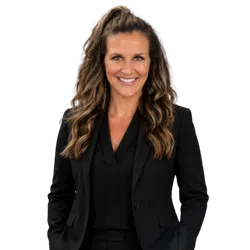 Smiling woman with long wavy hair wearing a black blazer and black top against a transparent background