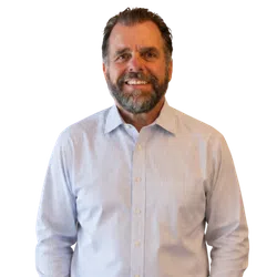 Middle-aged man with beard smiling, wearing light blue striped dress shirt against white background