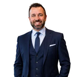 Smiling man in a navy blue suit with a tie and pocket square on a transparent background.