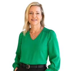 Portrait of a smiling woman with blonde hair wearing a green blouse, black belt, and silver jewelry.