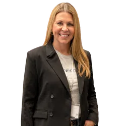 Smiling woman with long blonde hair wearing a black blazer and light shirt with badge around neck.