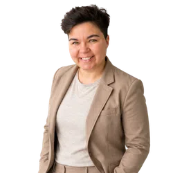 Smiling person with short dark hair wearing a beige blazer and light gray shirt against white background