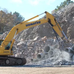 Komatsu PC360 LC excavator handling concrete debris and pipes at a construction excavation site in daylight.