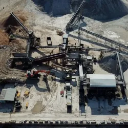 Aerial view of an industrial site with conveyor belts, machinery, gravel piles, and construction equipment.
