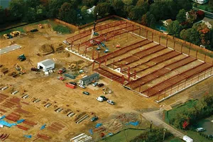 Aerial view of a construction site with steel framework being erected and various equipment scattered around.