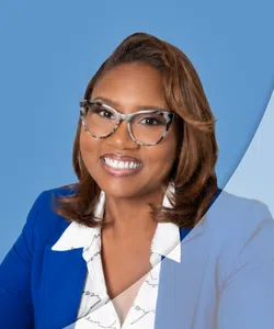 Professional woman with glasses wearing a blue blazer and white patterned blouse smiling against a blue background