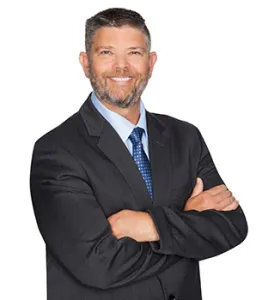 Confident businessman in a suit with crossed arms, smiling against a white background.