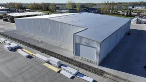 Large industrial warehouse with metal siding and concrete surrounding area with stacked construction materials.