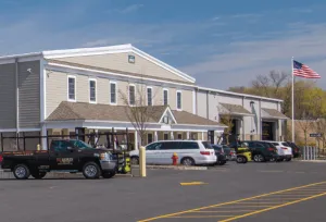 Commercial building with parking lot, multiple vehicles, an American flag, and clear blue sky in the background