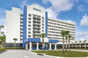Modern Hilton hotel building with white and blue exterior, palm trees, and clear blue sky in the background
