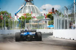 Race car on a city street track with safety barriers and a domed building in the background under a blue sky