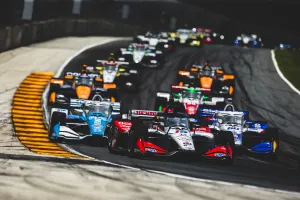 Multiple IndyCar race cars closely competing on a curved track during a high-speed race.