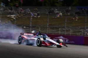 IndyCar race car drifting on track with smoke and blurred audience stands in the background