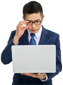 Young businessman in navy suit adjusting glasses while looking at a laptop screen with concern.