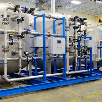 Industrial water treatment system with large metal tanks, pipes, valves, and control panels on a blue frame