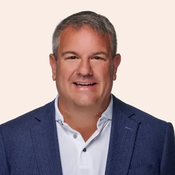Smiling middle-aged man with gray hair wearing a blue blazer and white polo shirt on light background