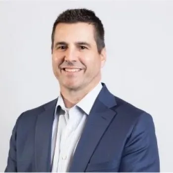 Professional man in a blue suit jacket and white shirt smiling against a plain white background