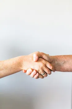 Close-up of two hands shaking in a friendly handshake against a plain background.