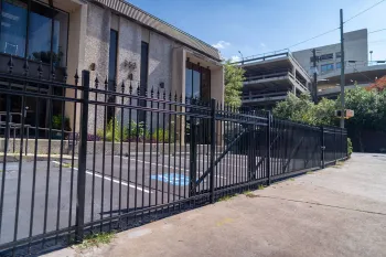 Modern commercial building with a black metal fence and accessible parking space under a clear blue sky.