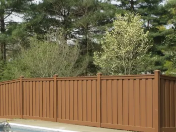 A brown wooden fence surrounding a pool with greenery in the background under a clear sky.