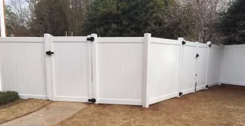 White vinyl fence with black hinges and a latch in a suburban backyard setting.
