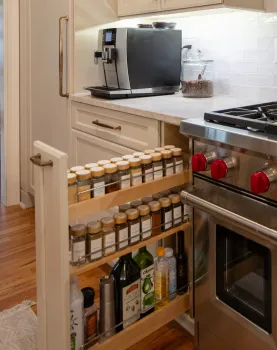 Modern kitchen corner with stainless steel stove, spice rack drawer, coffee machine, and white cabinets.