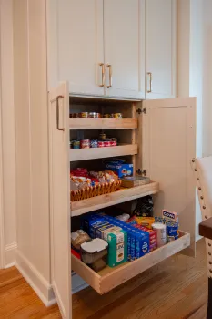 Organized kitchen pantry with pull-out wooden shelves holding canned goods, snacks, and boxed food items.