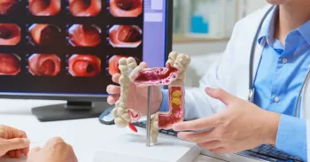 Doctor explaining colon health using anatomical model and colonoscopy images on screen in medical consultation.