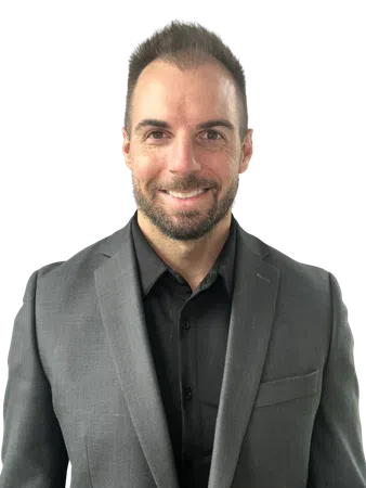Smiling man with short hair and beard wearing a gray suit jacket and black button-up shirt with no background